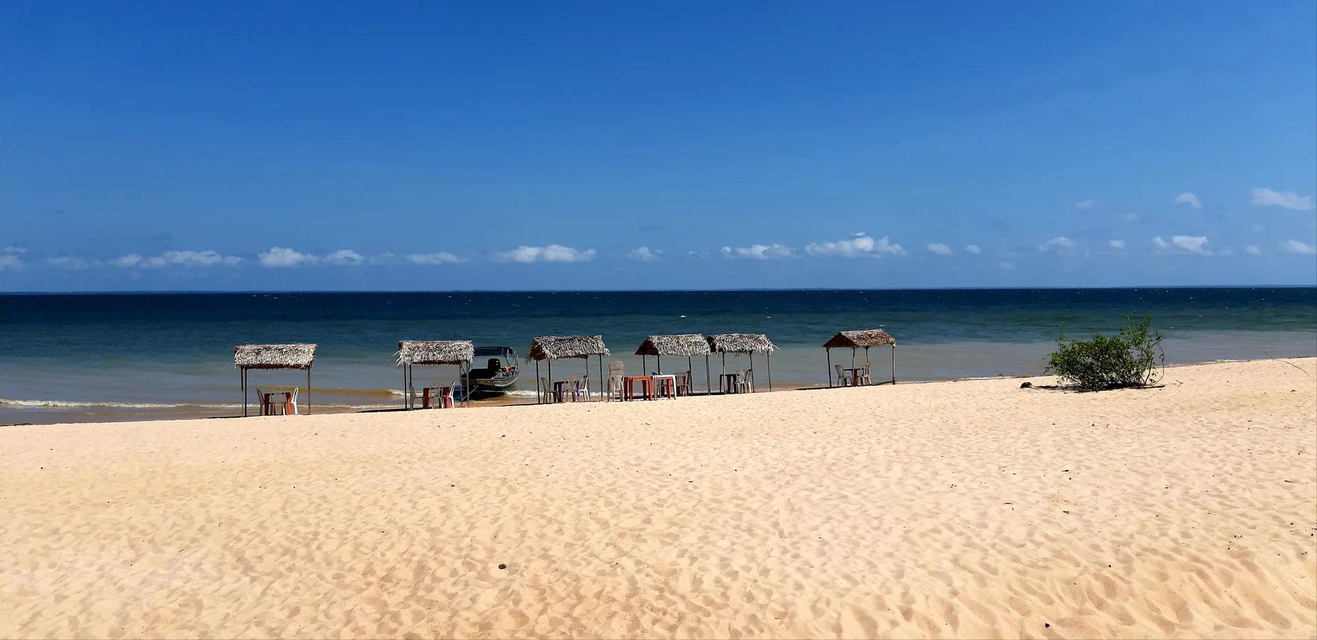 Sandy Tapajós beach with thatched shades, chairs and a boat at Alter do Chão