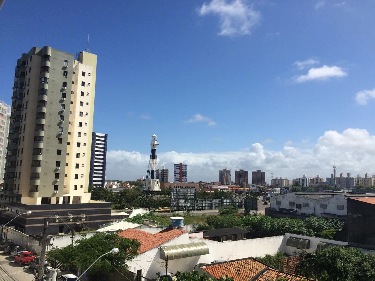 Residential towers, low rooftops and a lighthouse tower beneath a blue sky with clouds in Farolândia, Aracaju