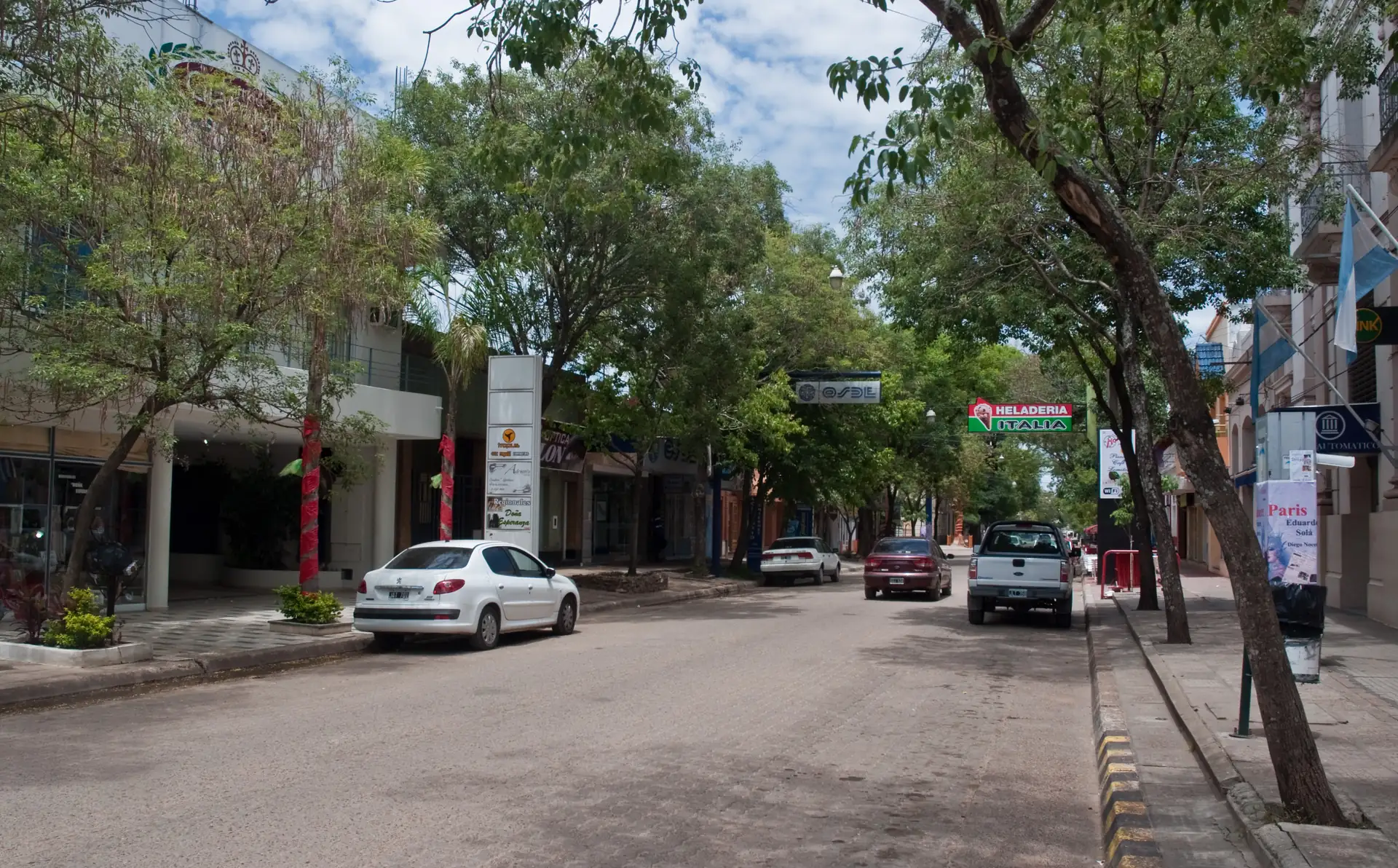 Tree-lined downtown street with shops and parked cars in Colón