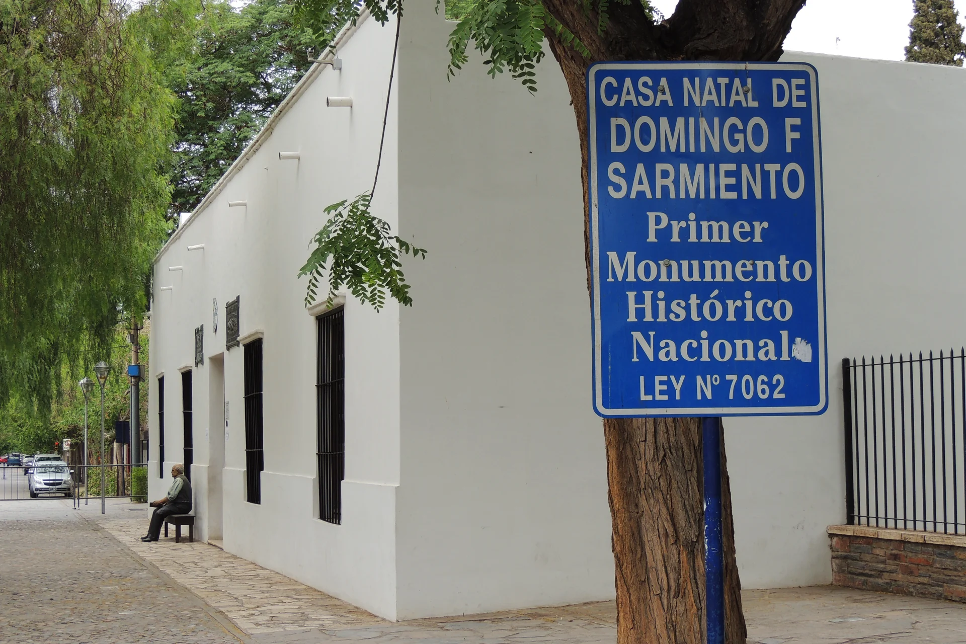 A white exterior wall and blue historic-monument sign at Casa Natal de Sarmiento in San Juan