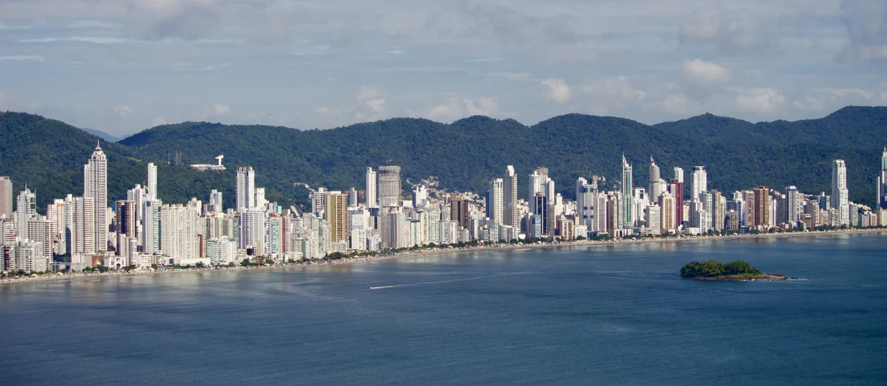 Balneário Camboriú waterfront towers, wooded hills and a small wooded island viewed across the sea