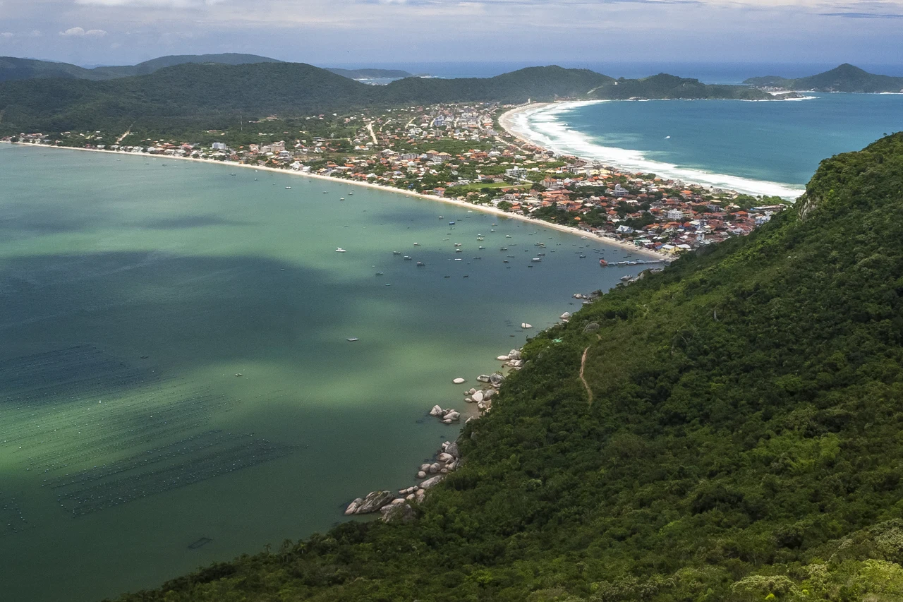 Historical coastal peninsula with houses, forest, sandy beaches, boats and blue water beneath clouds