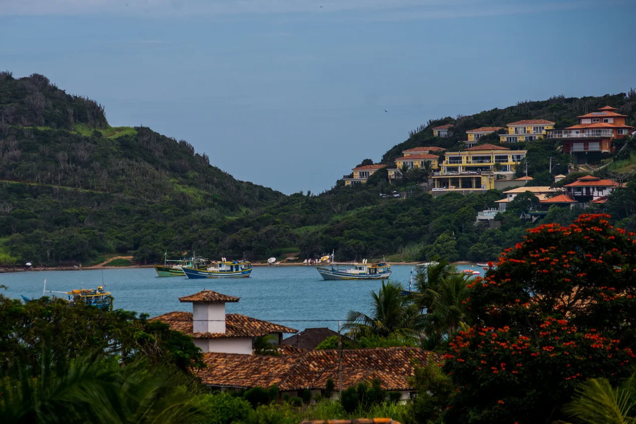 Fishing boats in a Búzios bay below green hills and buildings with tiled roofs