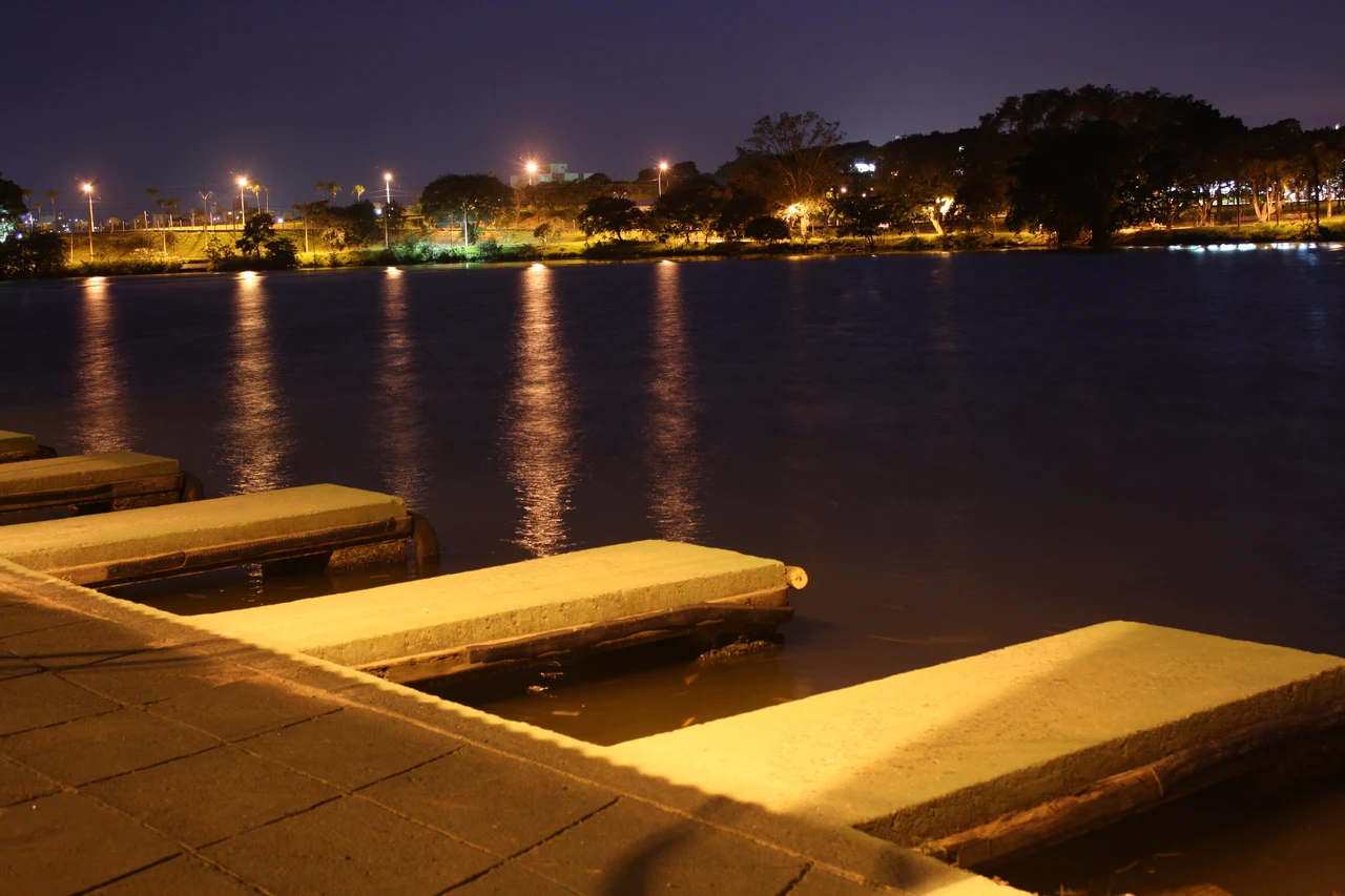 Historical lake at dusk with a foreground jetty, illuminated trees across the water and reflections beneath a dark sky