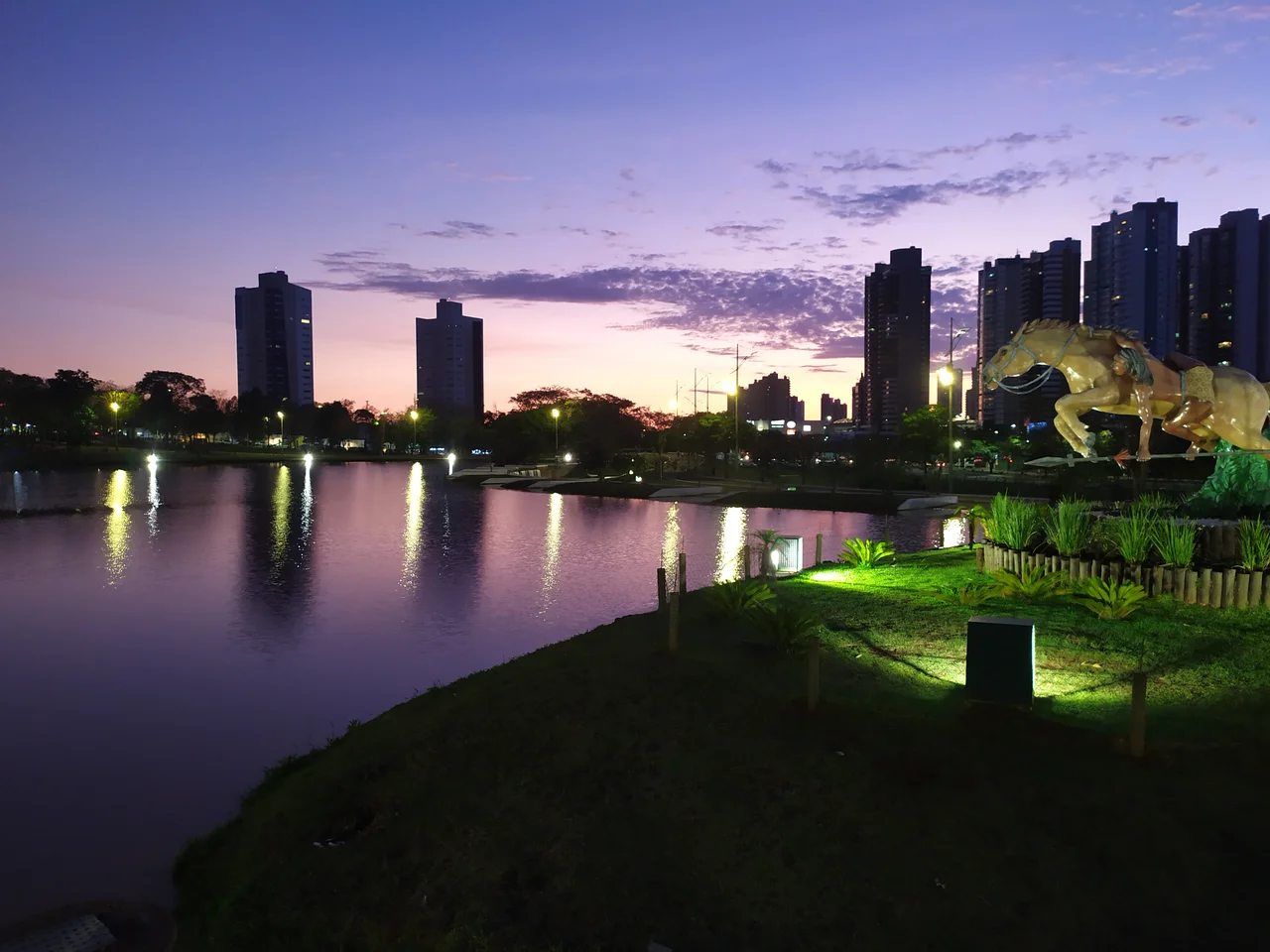 Lake, path and monument at Parque das Nações Indígenas in Campo Grande, with buildings in the evening background