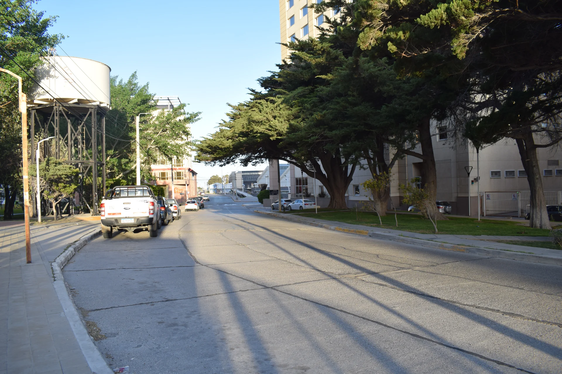 A Comodoro street lined with buildings and trees, with parked vehicles along the curb