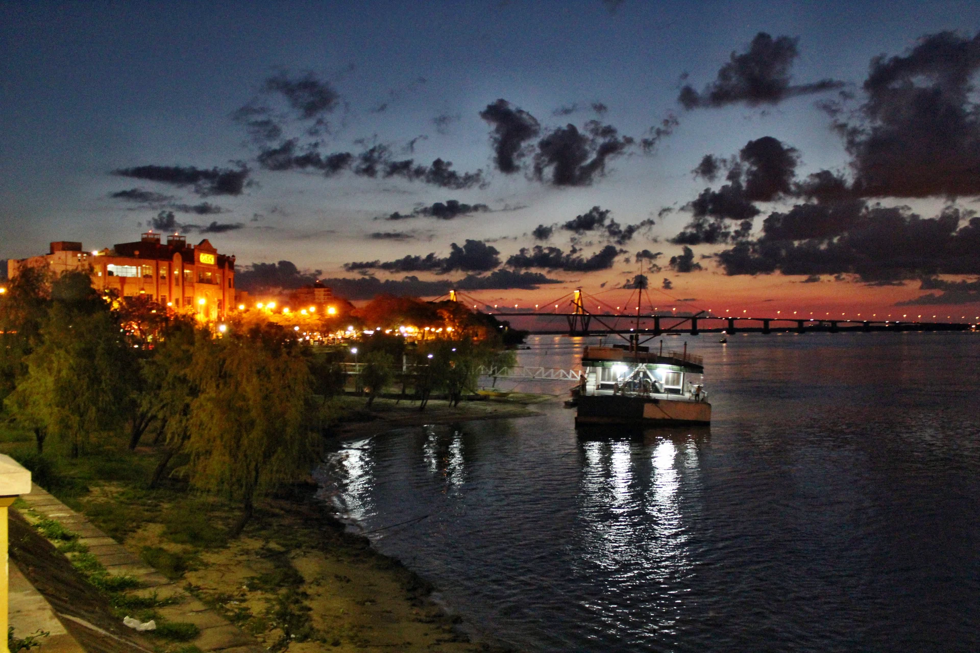 A boat beside the Corrientes riverfront at sunset, with a bridge and buildings in the distance