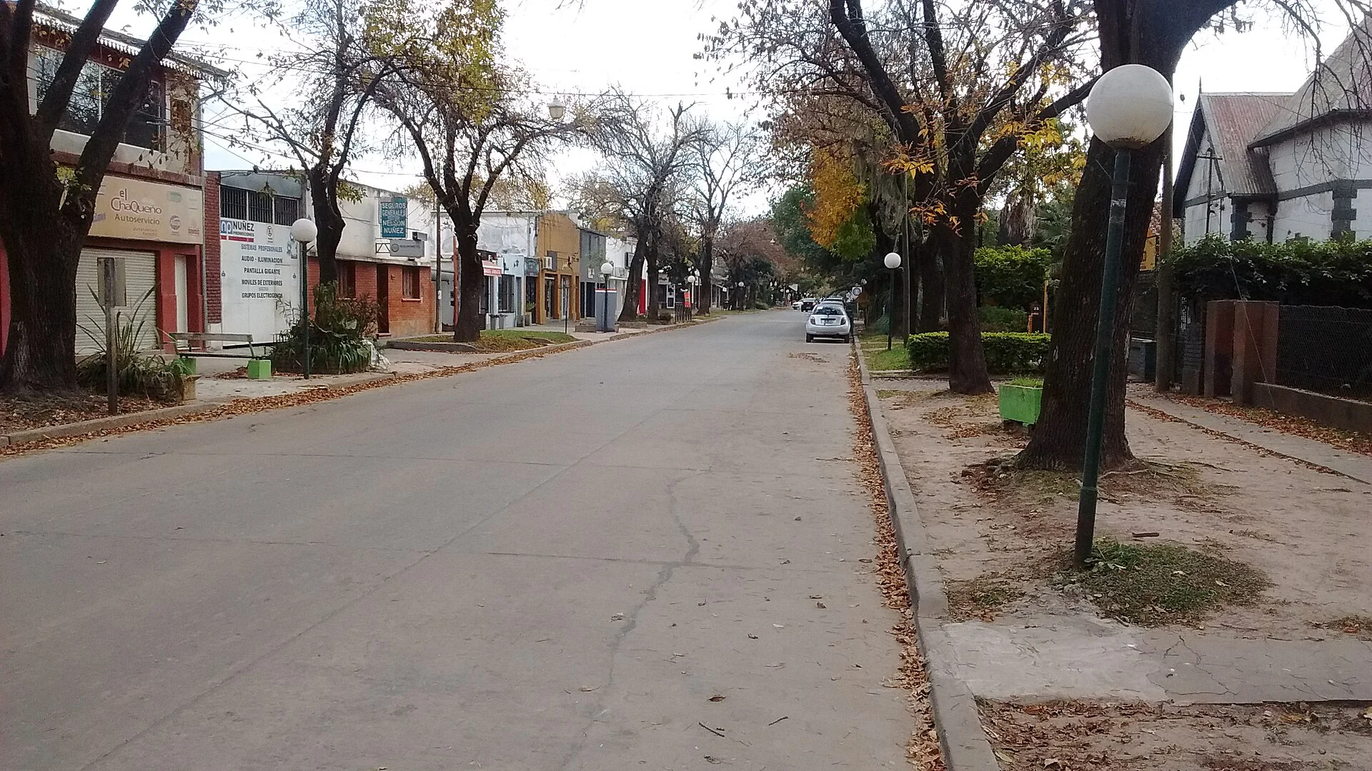 Santa Fe Street between Moreno and Yrigoyen in central Funes, with storefronts, trees and parked cars