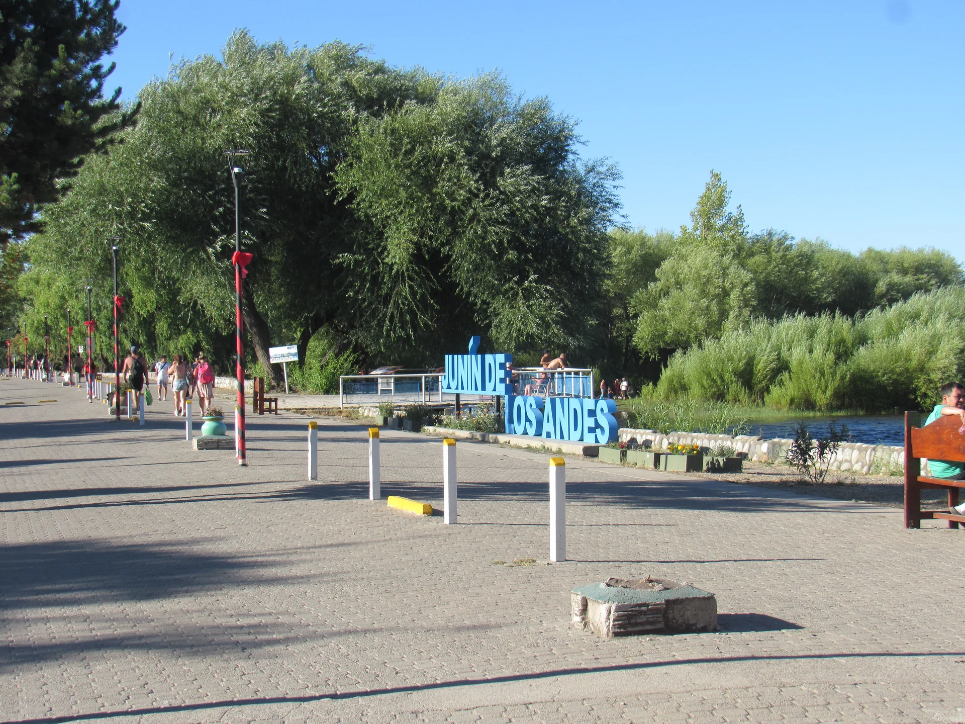 The Junín de los Andes sign beside the Chimehuín River, trees and a waterfront walkway