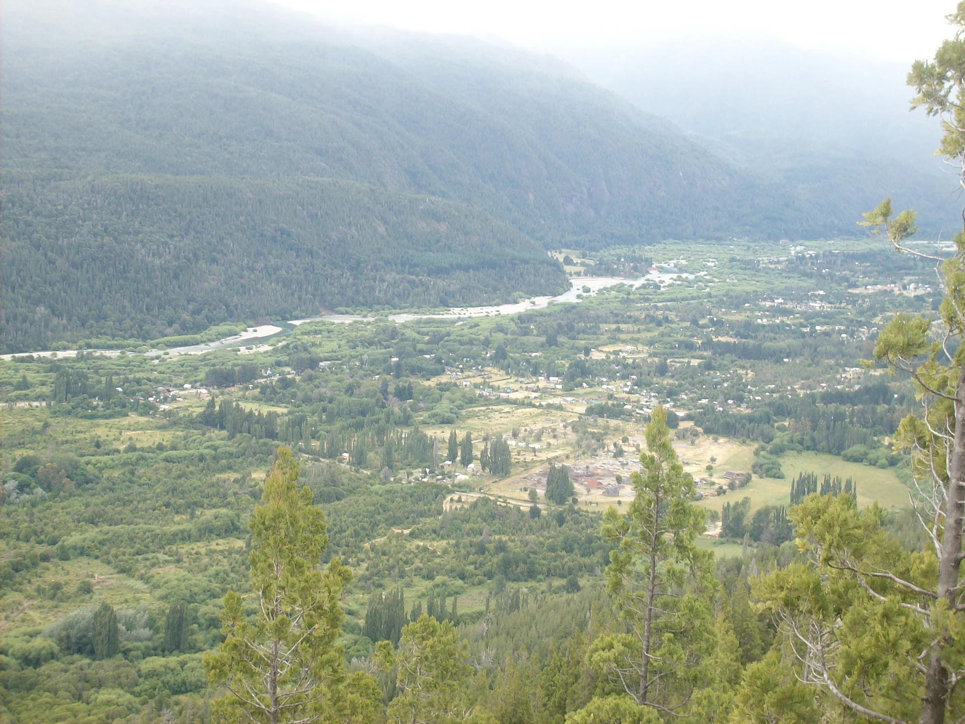 Trees, town buildings and a river below a wooded valley near Lago Puelo