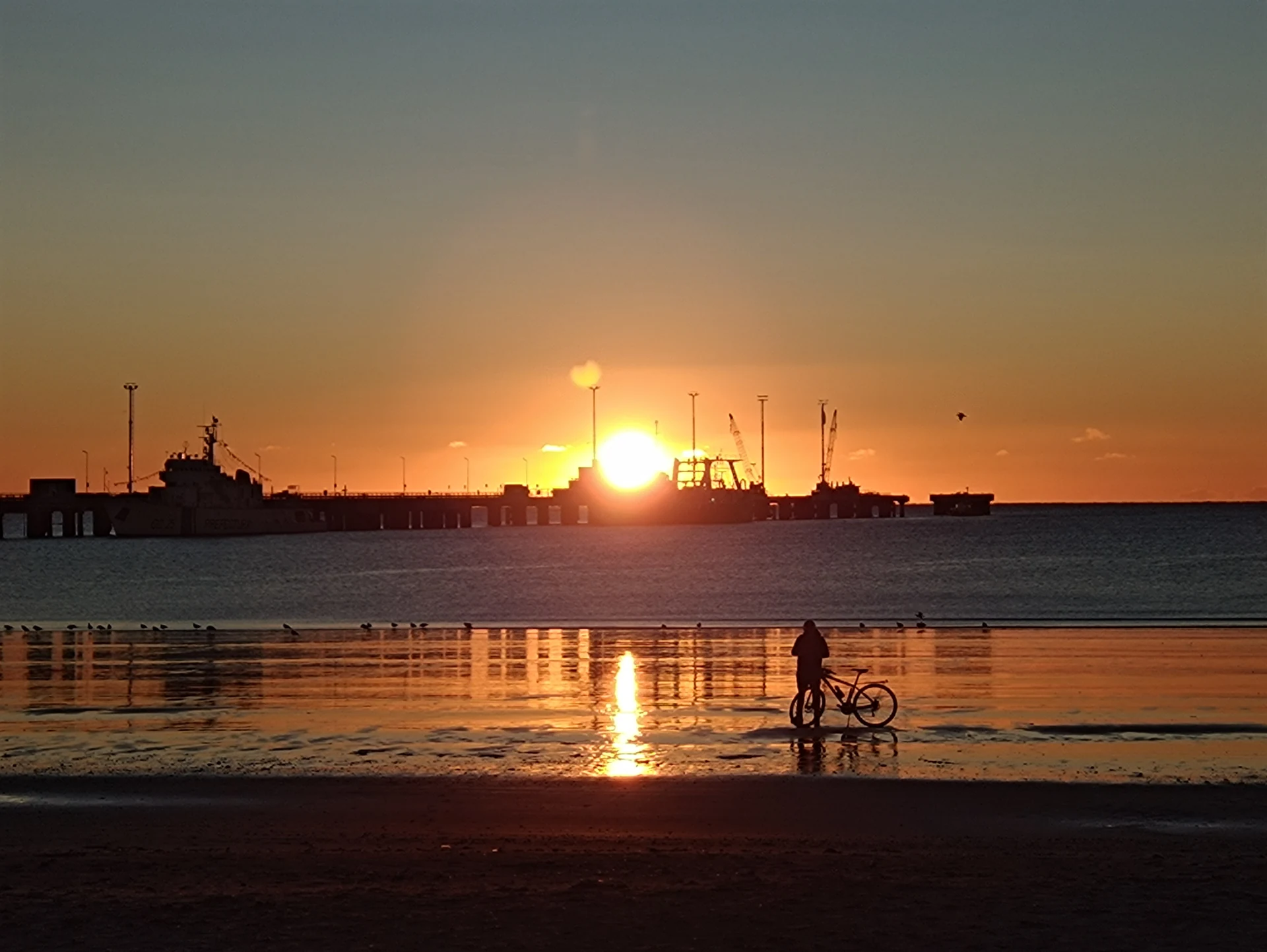 Sunrise over water, boats and a pier, seen from the Puerto Madryn shore