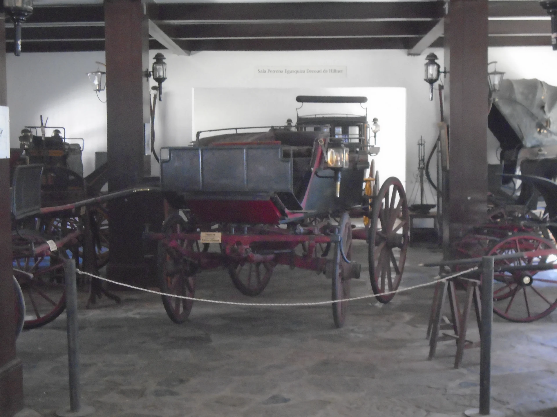 Historic horse-drawn carriages displayed indoors behind a rope at the Quilmes Transport Museum