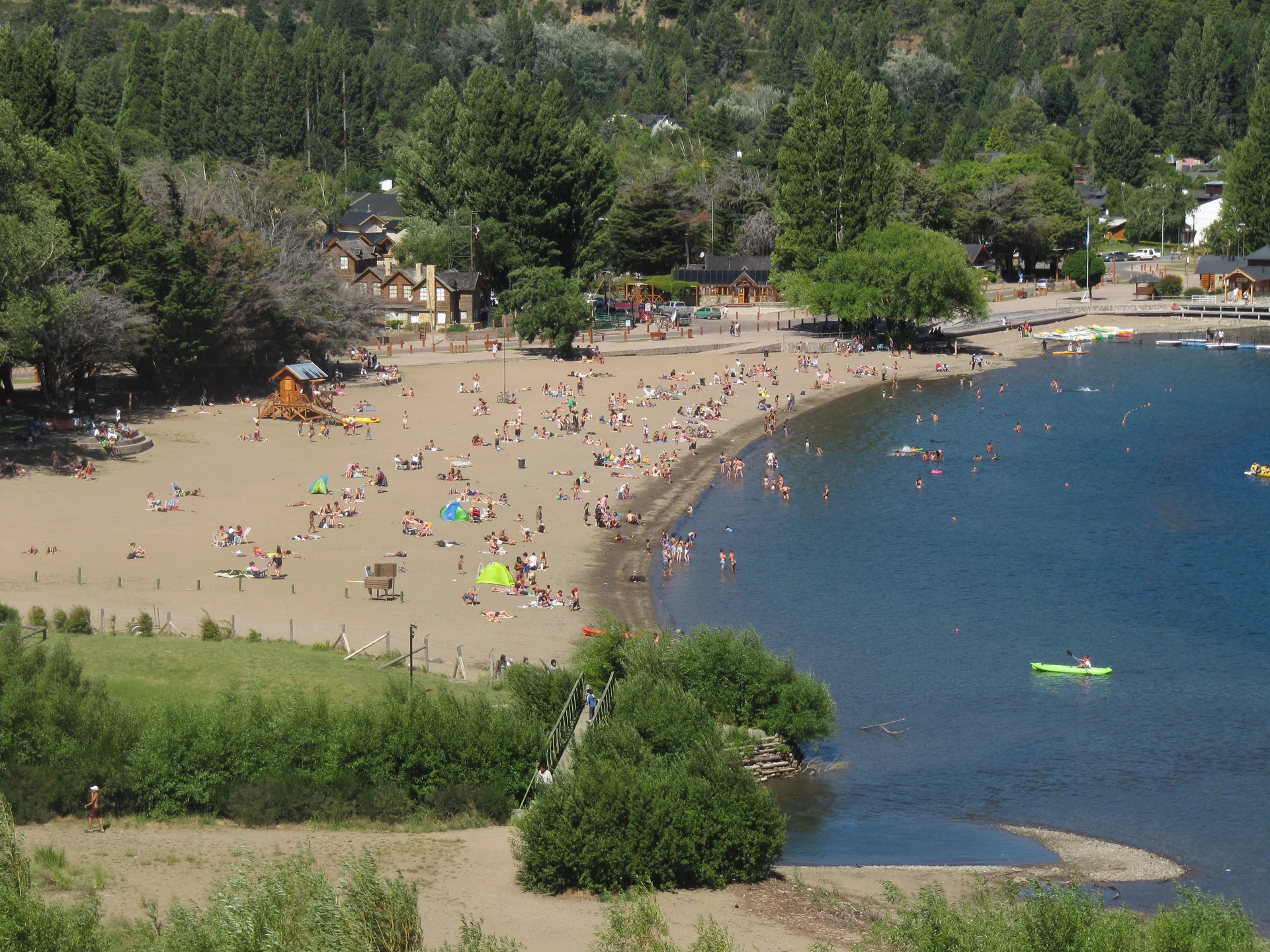 People on the shore of Lago Lácar with wooded slopes behind the San Martín de los Andes waterfront