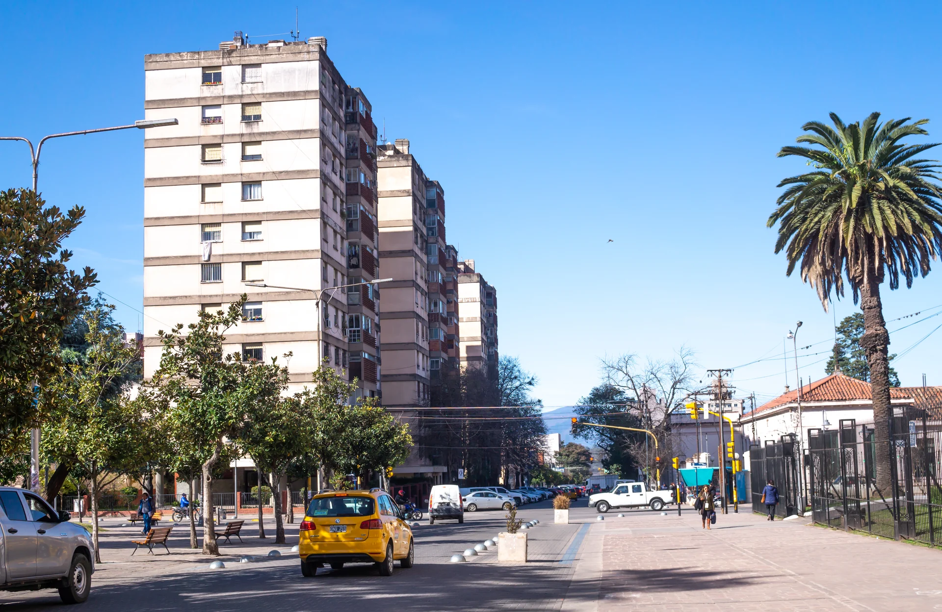 Apartment buildings, a palm tree, pedestrians and vehicles on San Martín Street in Jujuy in July 2018