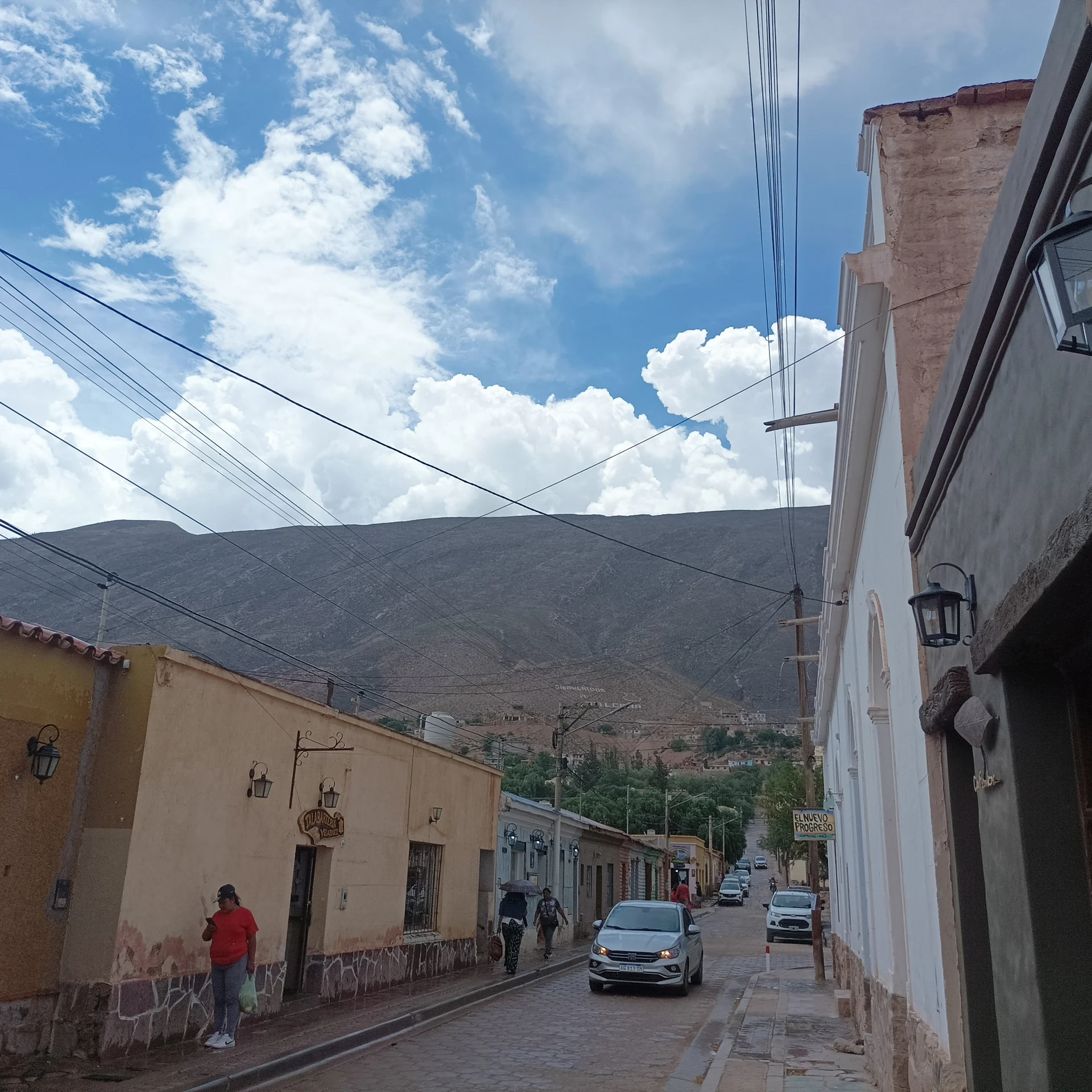 A stone street with low buildings, pedestrians, cars and mountains in Tilcara in February 2026
