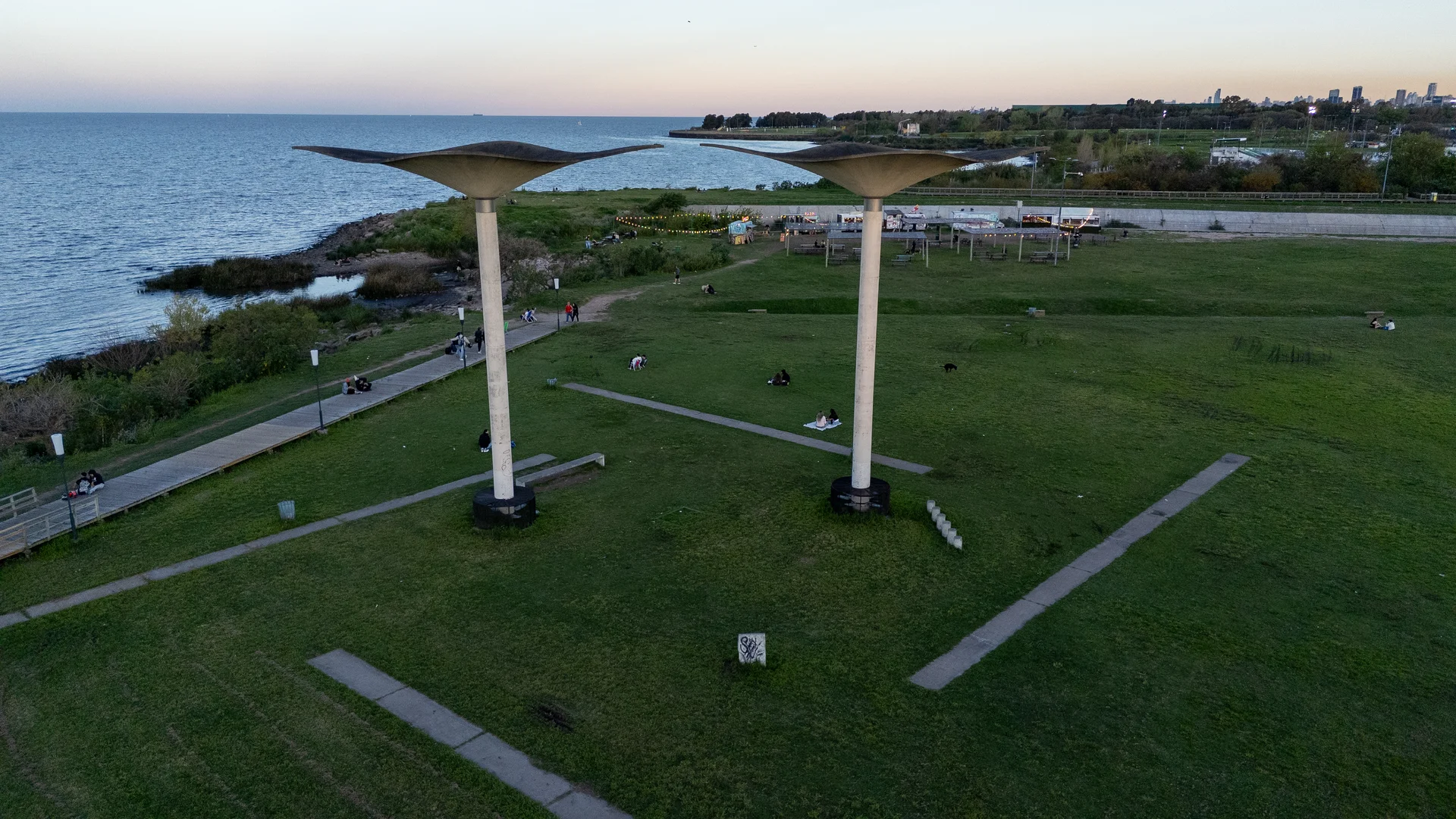 Paseo de la Costa paths, lawns and concrete shade structures beside the Río de la Plata in Vicente López, photographed October 1, 2025