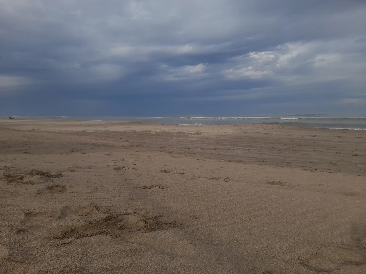 Wide sandy beach and low ocean waves beneath gray clouds at Paseo 121 in Villa Gesell
